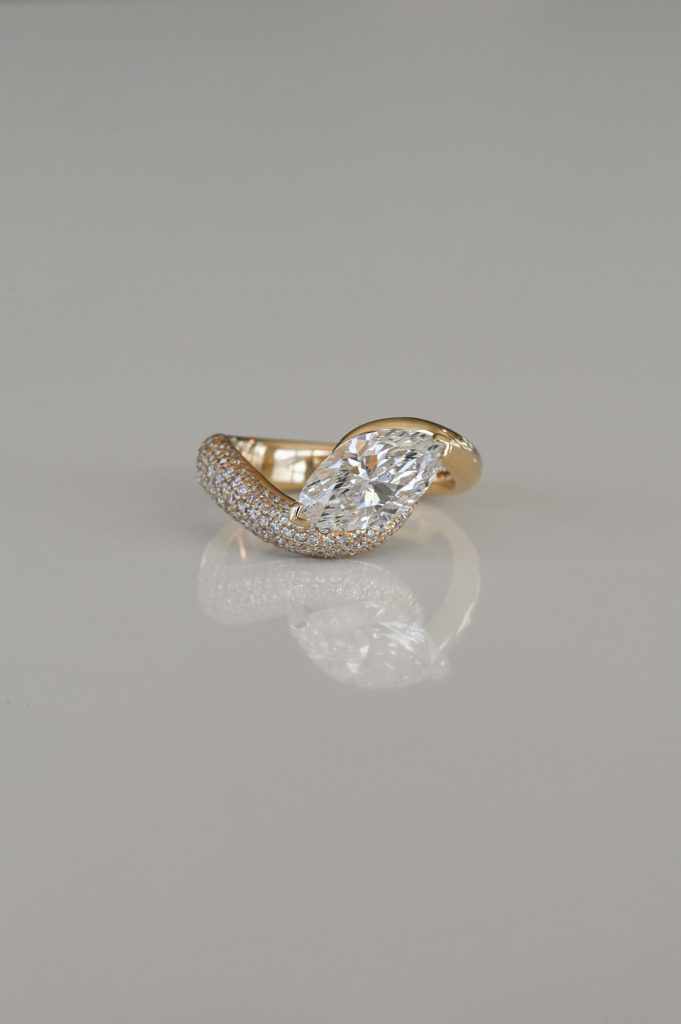 Yellow gold ring with a pear-shaped diamond center and pavé-set diamond band sweeping around one side.