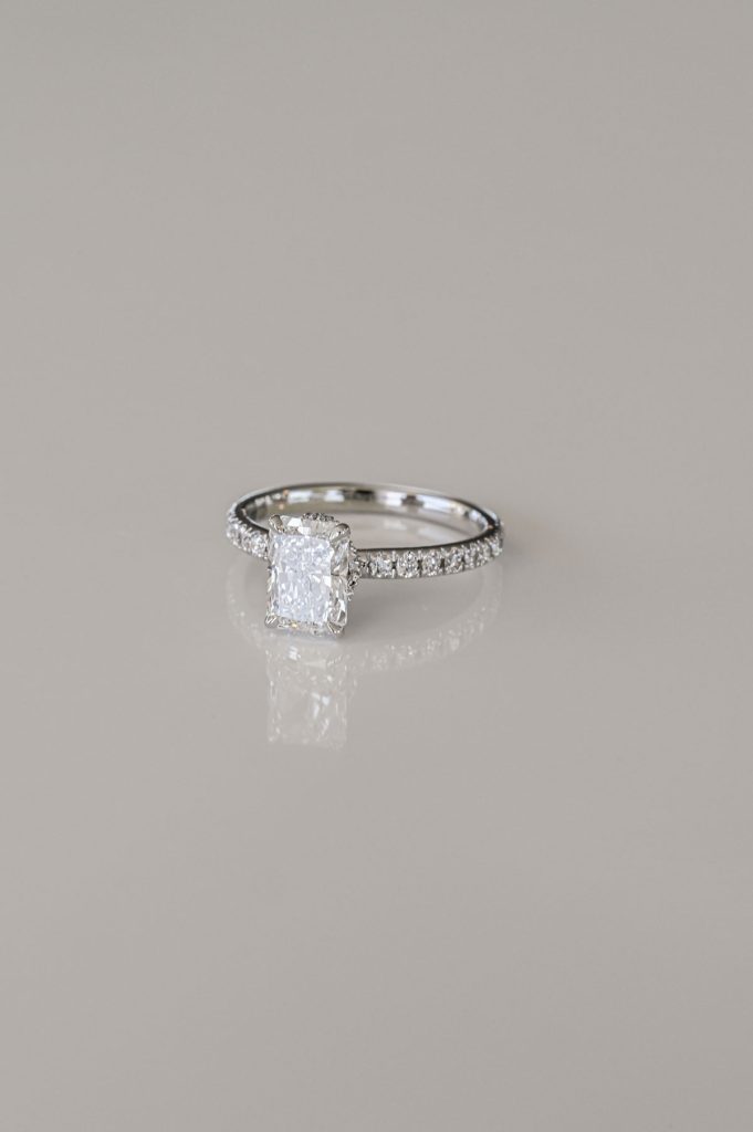 White gold ring featuring a radiant-cut diamond in a four-prong setting with a pavé diamond band.