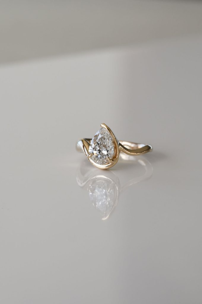 Yellow gold ring featuring a pear-shaped diamond in a modern bypass setting with a polished band.