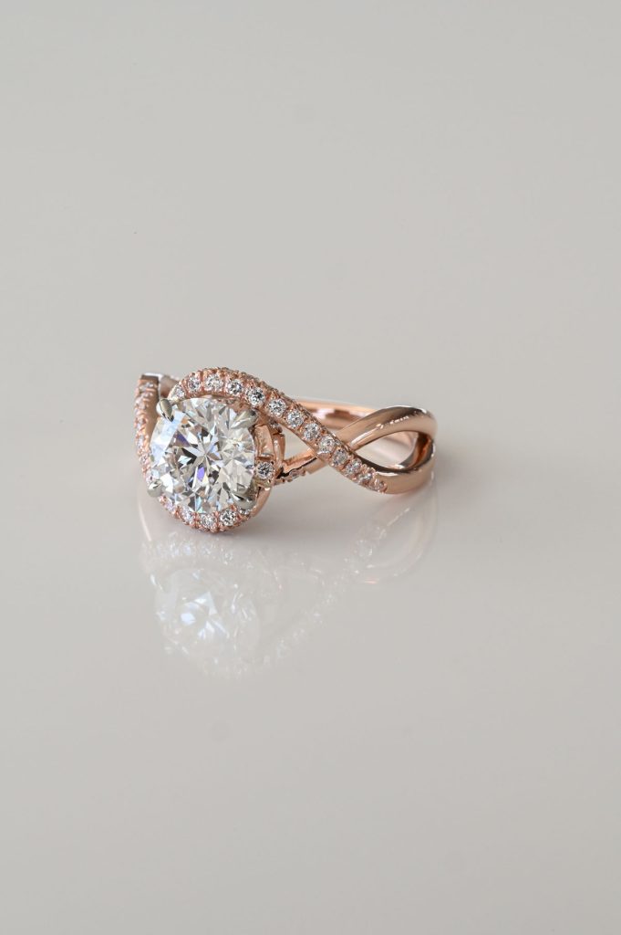 Rose gold ring with round brilliant diamond center and twisted pavé diamond band in an infinity design.