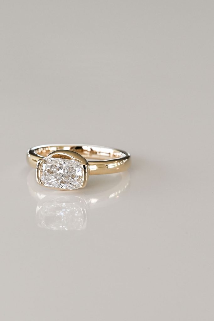 Yellow gold ring featuring a horizontally set cushion-cut diamond in a sleek semi-bezel setting on a polished band.